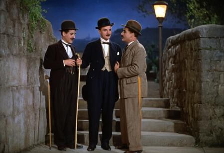 1931 Charlie Chaplin City Lights, color image depicts a classic scene with three men on a sidewalk at night. The layout is horizontal, with the subjects positioned in the foreground. On the left, a man with a mustache, wearing a bowler hat, a suit, and holding a cane, is tipping his hat. He has light skin and a distinctive expression. Next to him, another man, Charlie Chaplin, Chaplin's Tramp, also with light skin, dressed in a tuxedo and top hat, is leaning slightly and smiling. Both men are interacting with a uniformed officer standing on the right, who has his hands on his hips and is holding a baton. The background features a stone wall and steps, with a lamppost providing illumination. The overall atmosphere is reminiscent of early 20th-century cinema. 1930s movies style