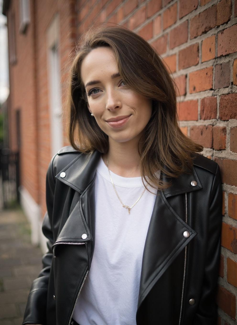 An exciting professional photograph of a 20yo young woman CiOD, wearing a leather jacket and white tshirt, standing in front of a brick wall, smile, pale skin, striking makeup, lipstick, detailed skin, bokeh, natural lighting, female focus, SFW, Instagram<lora:Ciara_ODoherty-000018:1>