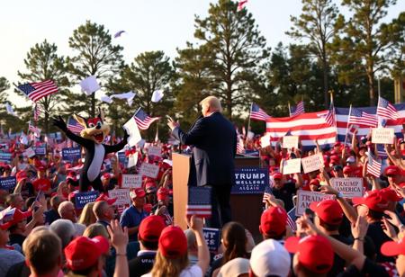 Donald Trump standing on stage at a lively political rally in Alabama, with the iconic Tasmanian Devil from cartoons beside him. The rally is packed with a large, energized crowd waving American flags, many wearing red ‘Make America Great Again’ hats. The stage is surrounded by large banners and signs with bold political slogans, while the Tasmanian Devil spins wildly, causing papers and flags to fly around. Trump, with his signature gesture, is delivering a speech, while the crowd cheers, a mix of excitement and chaos unfolding as the cartoon character creates havoc nearby. The setting is a classic Southern backdrop with tall trees, and the golden evening light casting a glow over the scene.
