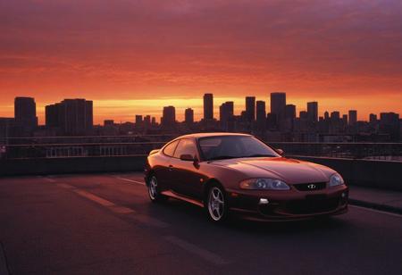 (1996 Hyundai Tiburon RD) motor vehicle, no humans, city, sky, outdoors, scenery, orange sky, road, building, cityscape, sunset, vehicle focus, skyscraper, sports car, shadow, gradient sky, red sky, evening, cloud, street, skyline, twilight, spoiler \(automobile\), orange background, dusk, red background, water, solo, bridge,