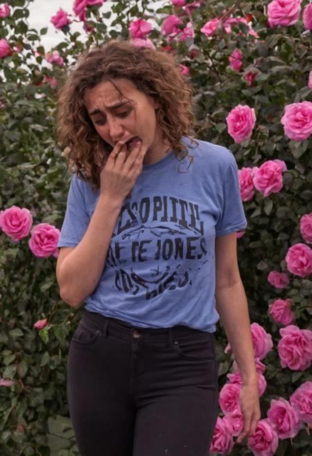 crying style, a woman with brown curly hair and purple eyes wearing a blue t-shirt and black pants weeping over pink roses,