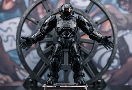 The image features a highly detailed, full-body view of a Neo Bubbleman, exuding an aura of advanced technology and precision, predominantly black and gray, stands boldly on a clear stand, arms outstretched in a ready stance. A camouflage pattern adorns the Neo Bubbleman's body, adding a sense of realism. Placed in front of a Cannon Wheel, the dark color scheme creates a striking contrast. A vibrant, detailed background enhances the composition.