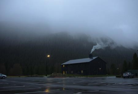 A dark building, built into the mountainside, foggy, rainy, parking lot, evening, overcast, looming,