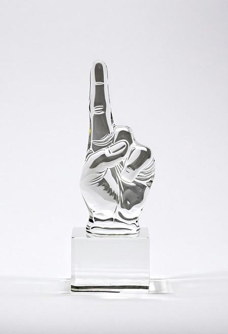 A clear glass sculpture of a raised fist showing the middle finger
