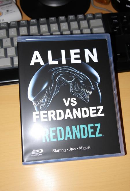 This is a photograph of DVD case with a desk background. The case features an alien and a xenomorph as in alien vs predator movie and a prominent black bold text "Alien VS Fernandez", Below is a bullet list of features: "Starring", "Javi" and "Miguel".