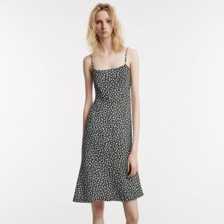 straight look and she is looking directly at the camera with a serious expression. The background is plain white., The image shows a young woman standing in a studio with a white background. She is wearing a black and white floral print midi dress with thin straps and a ruffled hemline. The dress has a fitted bodice and a flared skirt that falls below her knees. The woman is also wearing black strappy heels. She has shoulder-length blonde hair styled in loose waves and is looking directly at the camera with a serious expression.