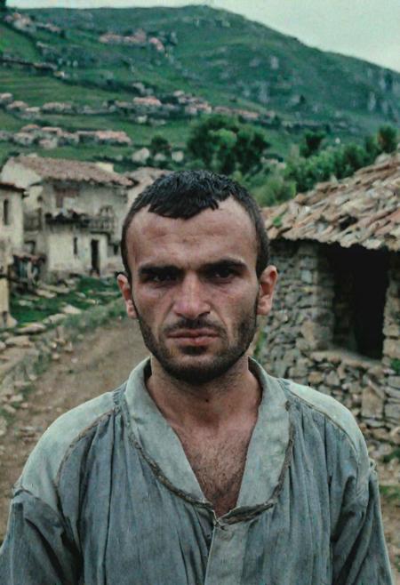 A albanian 30 year old man standing outside in a village with hills in the background