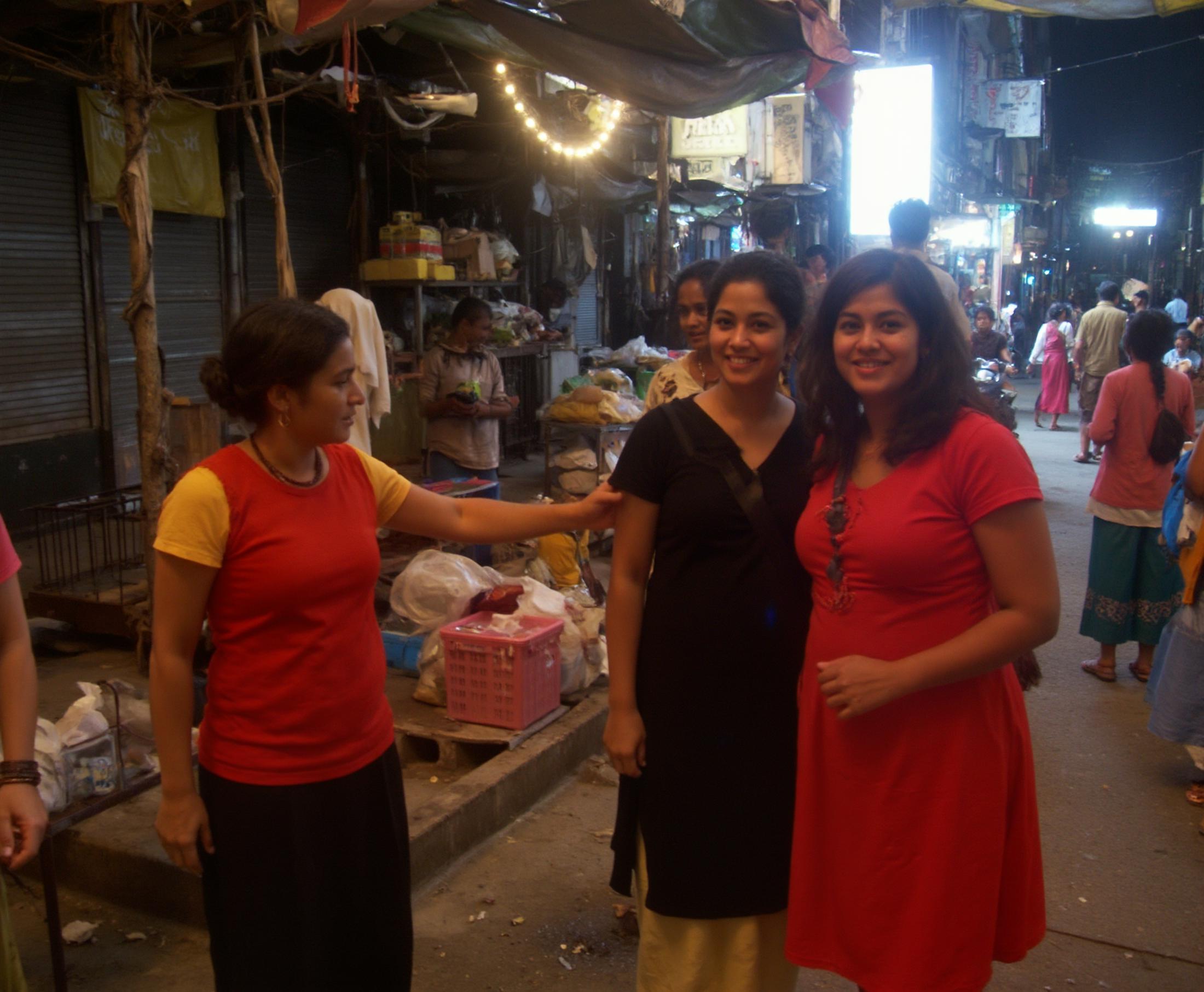 Amateur photography of two women posing in brightly lit street in india, cluttered background, overexposed <lora:amateurphoto:1>