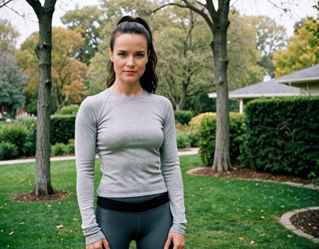 ((analog)) raw documentary photo of a good-looking American woman, age 40, characterized by white pale skin and medium black hair styled in a sleek ponytail. She has a slender figure with ((wide hips)) and (large ass), displaying a confident expression, dressed in a gray Long-sleeve running top and running shorts, standing with arms relaxed, full-body shot, high angle, in a park setting, shot on a Nikon F6 camera with film grain, under overcast lighting, (in the style of Lauren Greenfield).