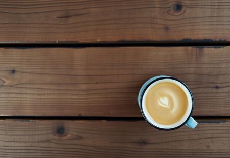 A view from the top of a wooden table with a coffee mug, classic stock photo, chill vibe, latte cafe on a rustic wooden kitchen table. Empty table except the coffee mug. Coffee mug on the right. Clean mug with fresh coffee, light foam on coffee. Tiny space between plank.